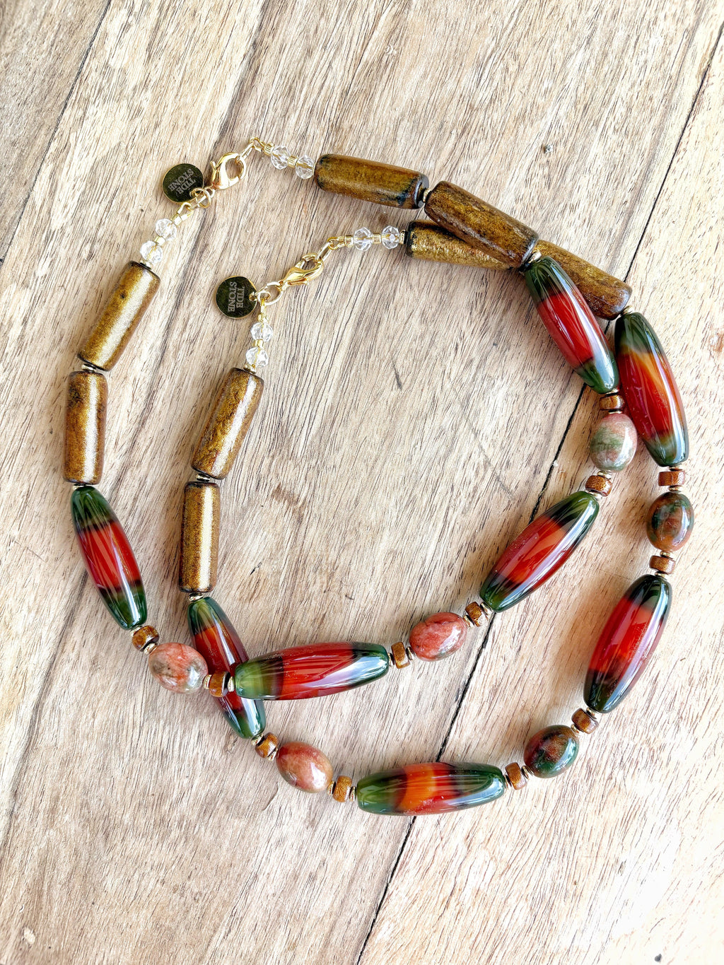 Collar corto artesanal de piedras semipreciosas en tonos marrón y rojo con detalles verdes, cierre metálico dorado, joyería.